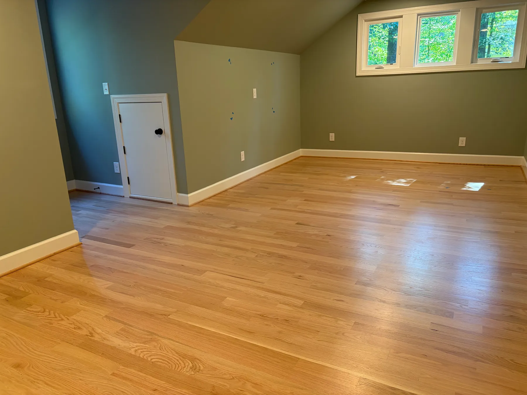 Wide view of a finished Brown project room with light wood flooring, recessed lights, and three high windows