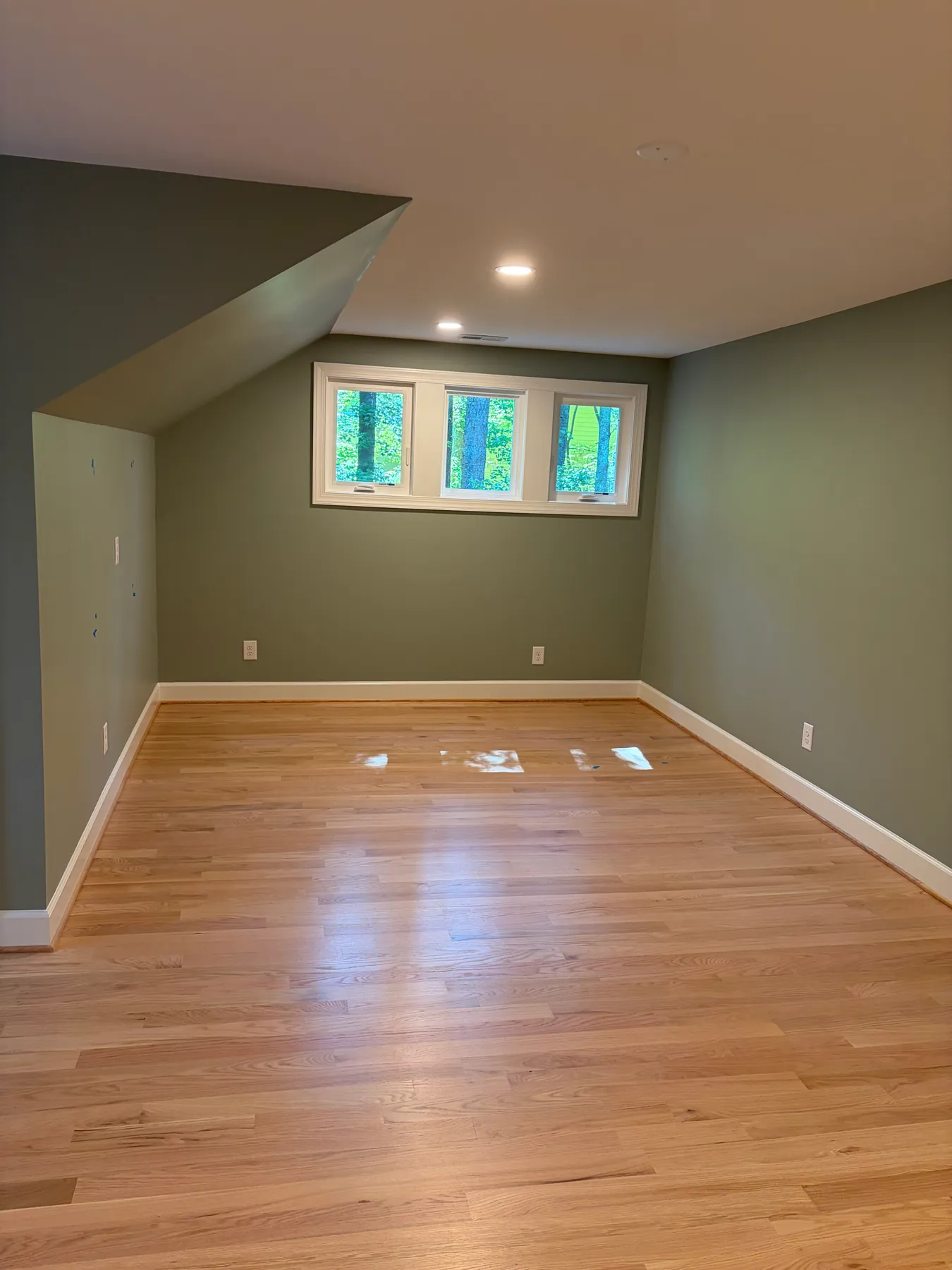 Finished Brown project room with light wood flooring, recessed lights, and three high windows