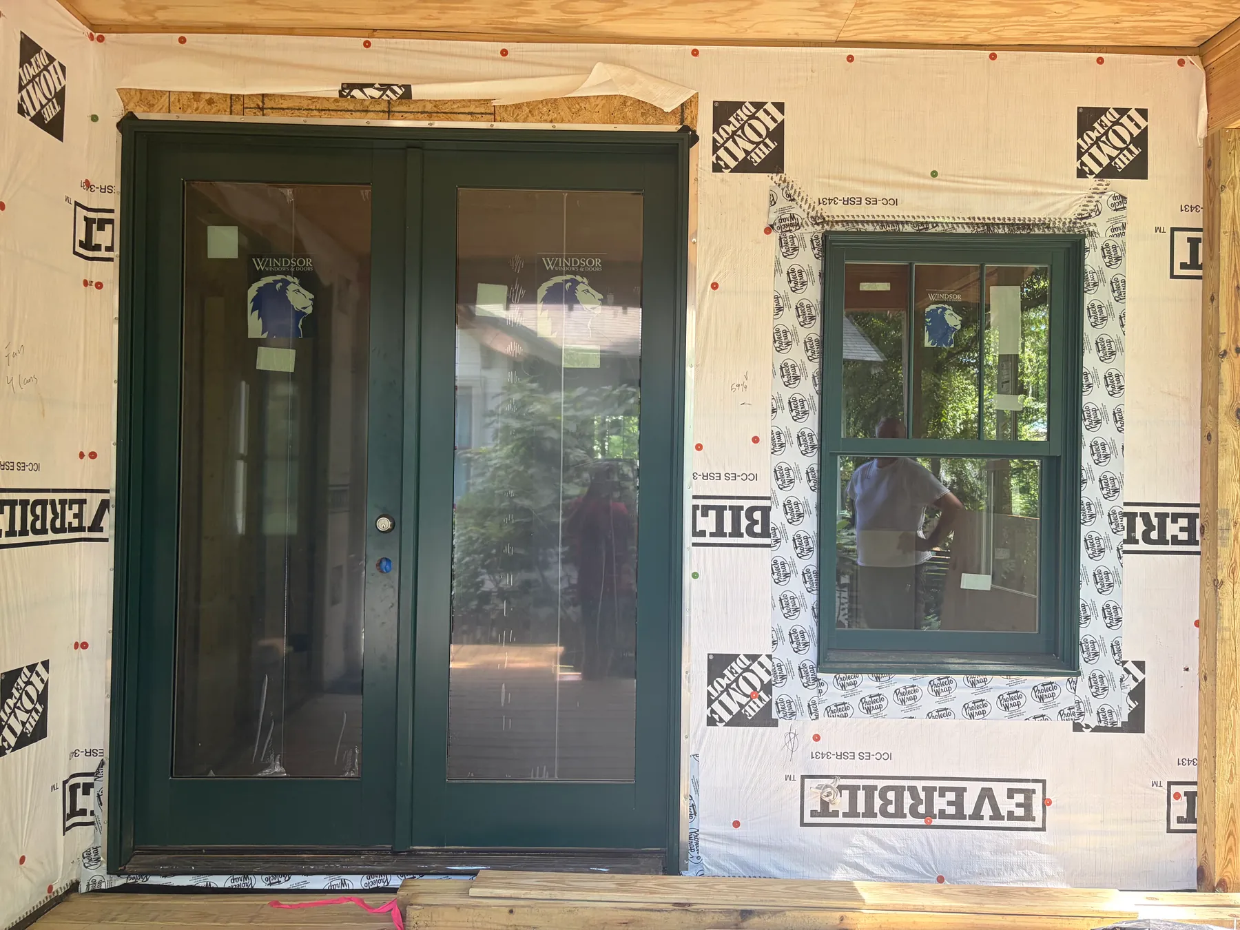 Front view of newly installed dark green double doors and window surrounded by exposed weather barrier on the Janet addition