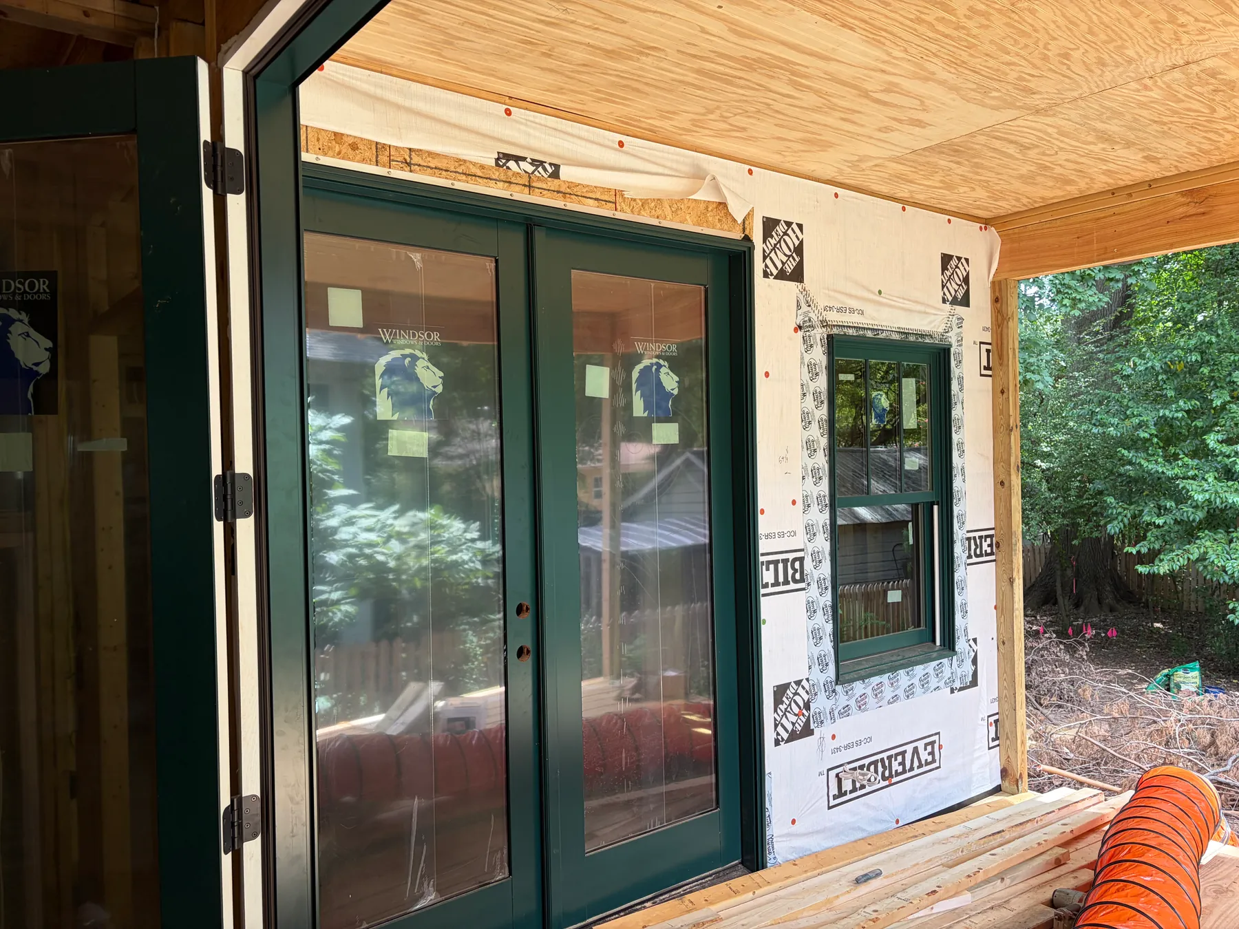 Angled view of newly installed dark green double doors and window within exposed exterior wall sheathing on the Janet addition